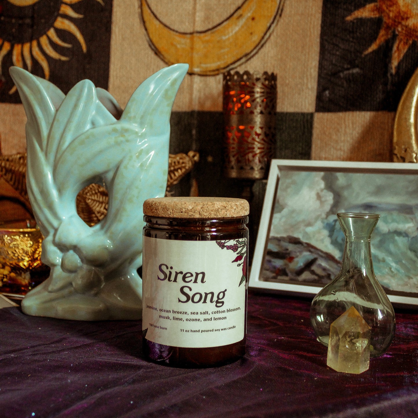 Jar labeled 'Siren Song' on a table with mystical decor including a mask and candles.