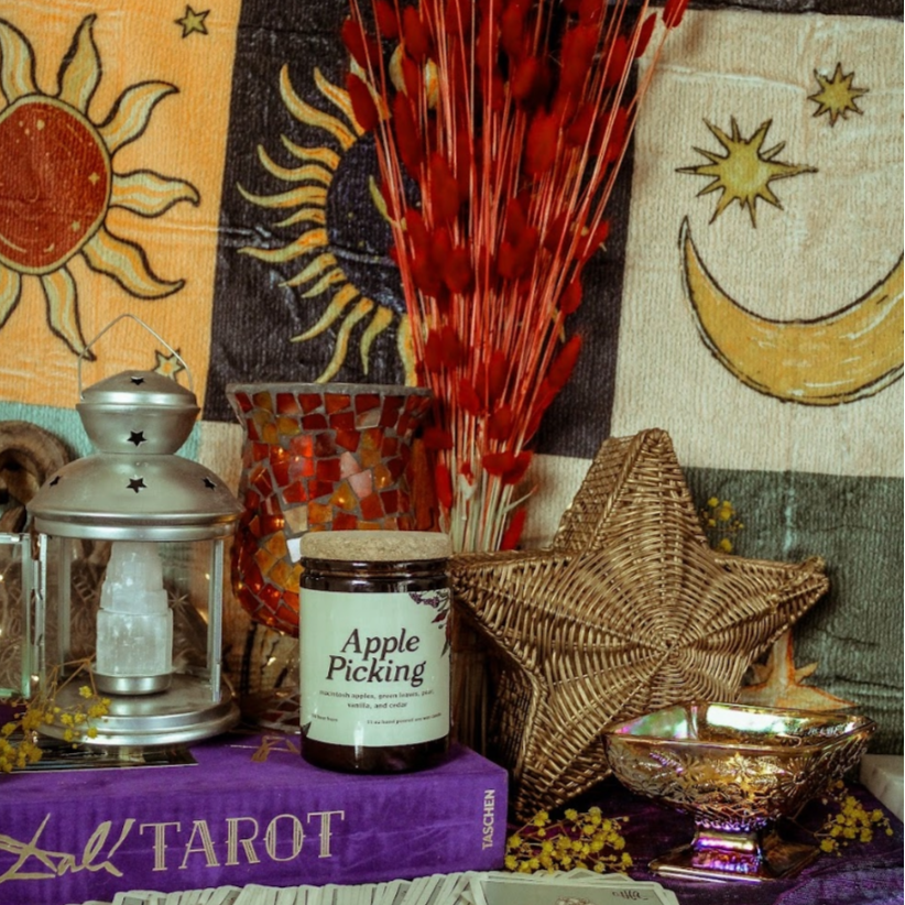 Wiccan or spiritual items including tarot cards, candles, and a jar on a purple cloth with star and moon designs.