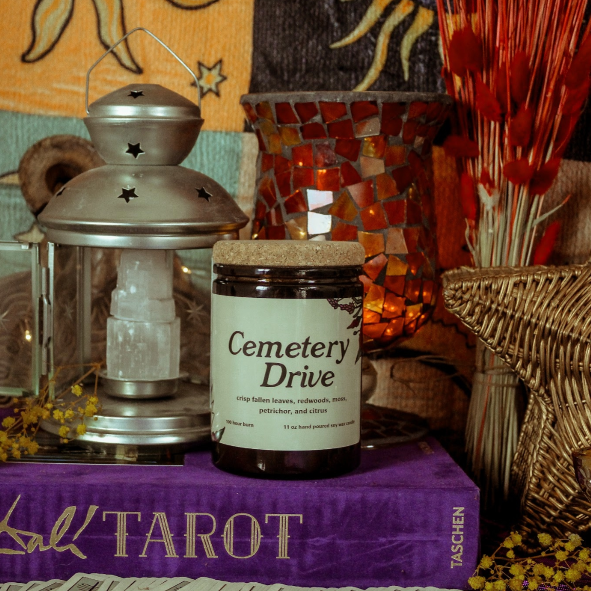 Candle labeled 'Cemetery Drive' on a tarot book with decorative items.