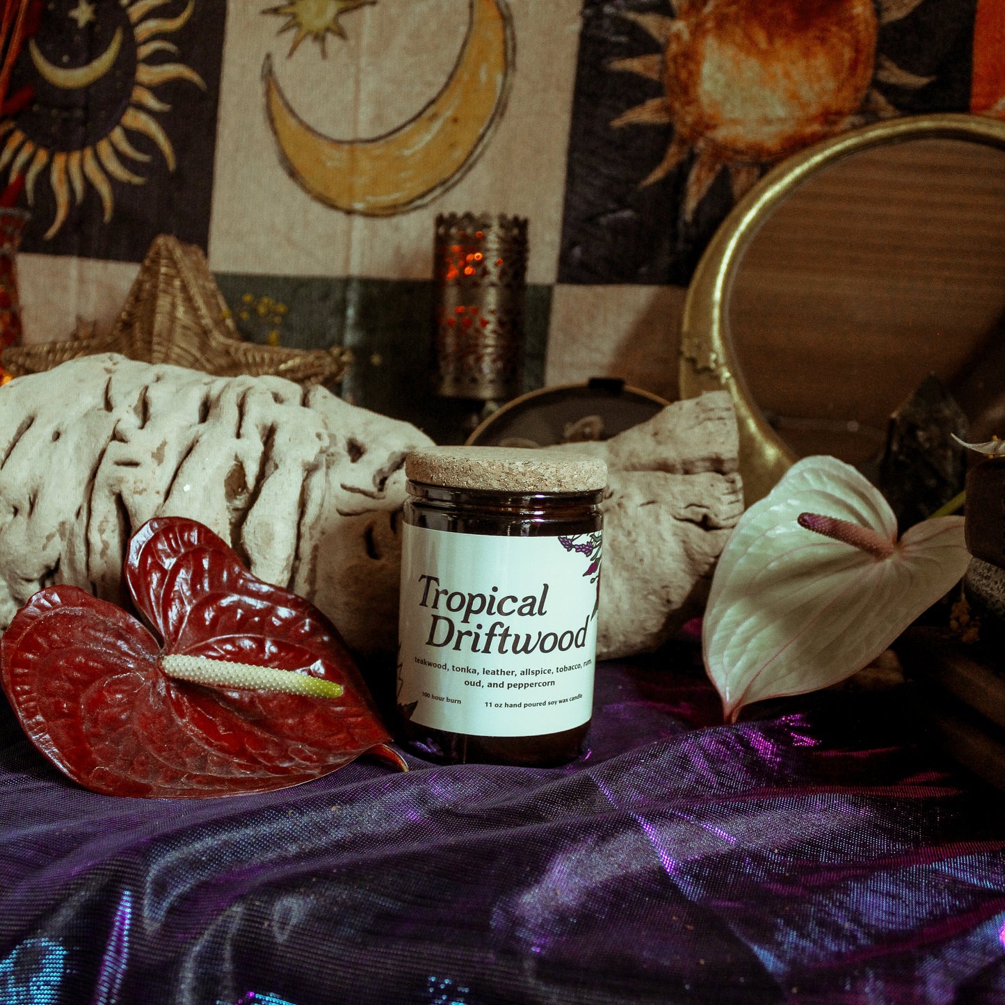 Jar of 'Tropical Driftwood' candle on a tablecloth with decorative elements and candles in the background.
