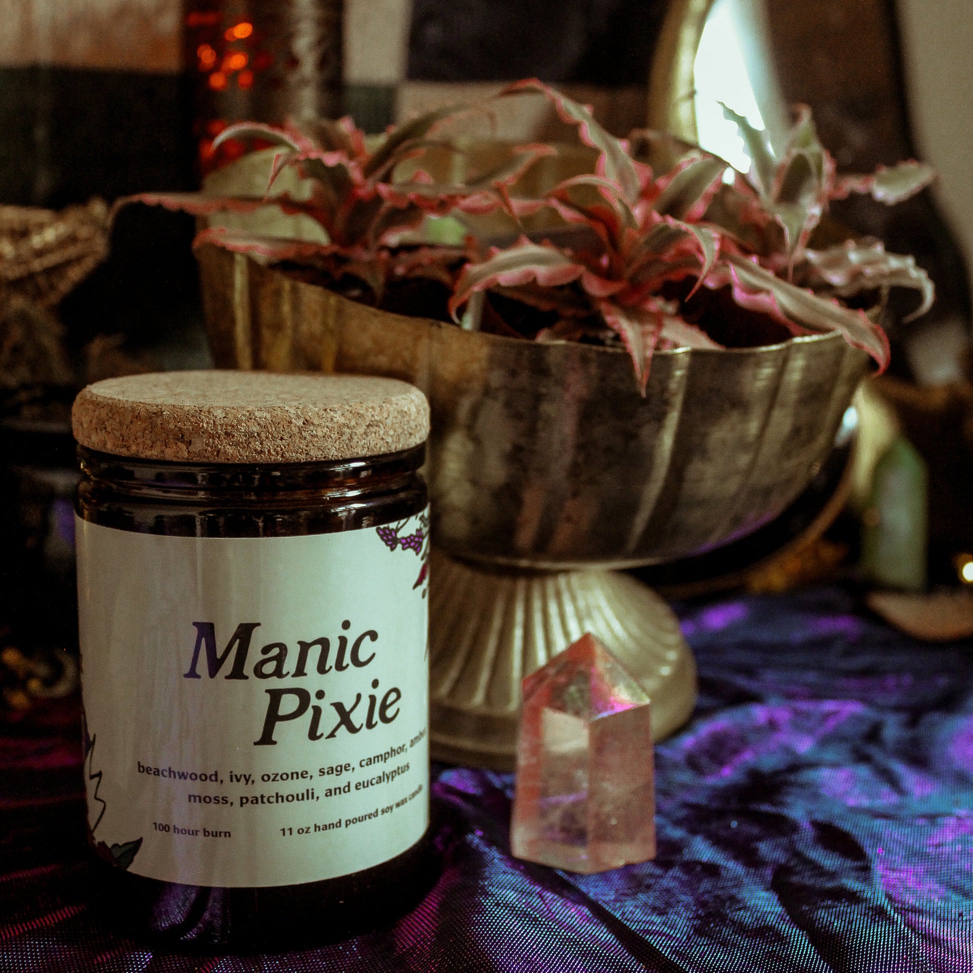 Jar labeled 'Manic Pixie' on a table with decorative plants and crystals.
