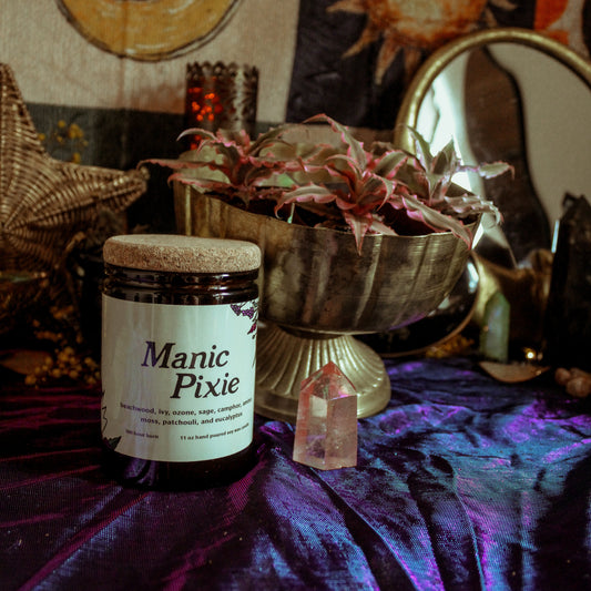 Jar labeled 'Manic Pixie' on a mystical table with candles, crystals, and decorative items.