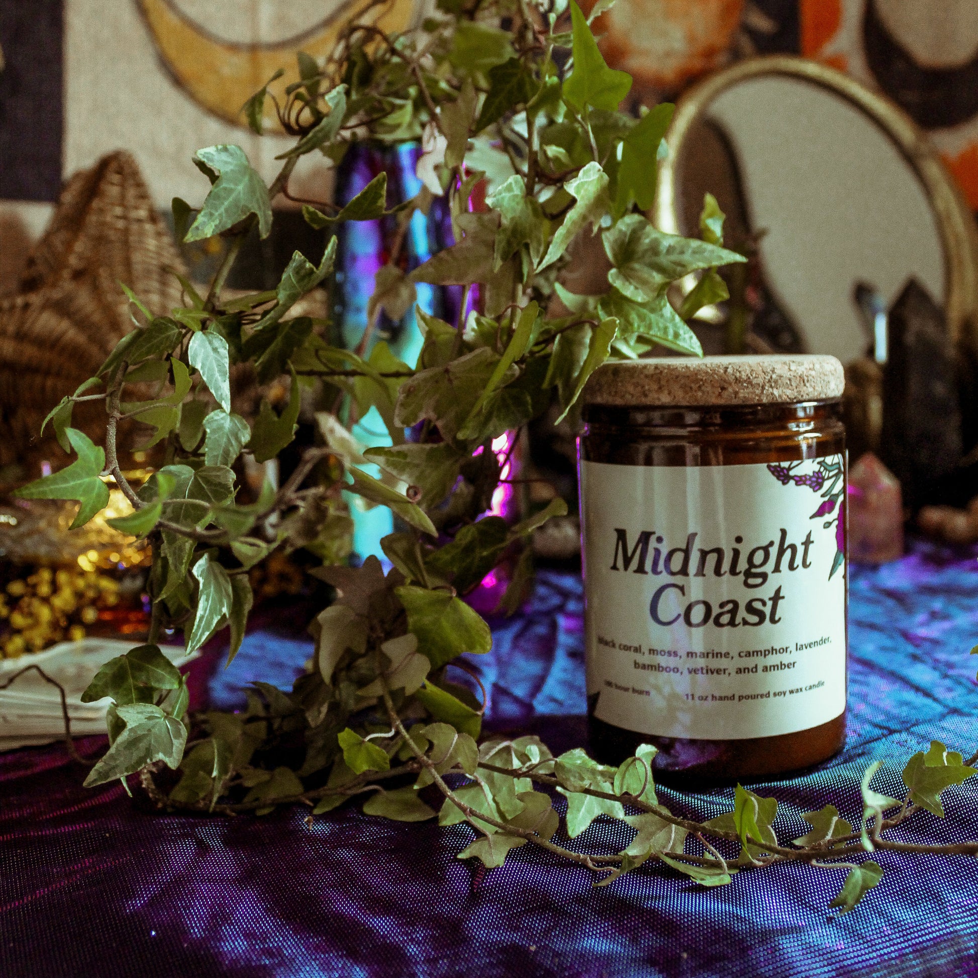 Jar of 'Midnight Coast' on a table with plants and a colorful tapestry in the background