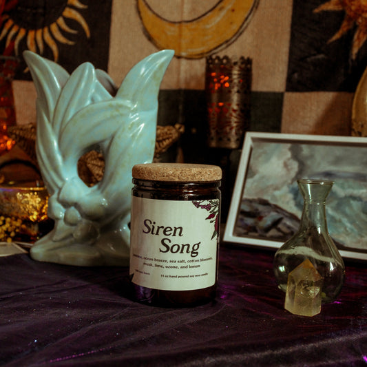 Jar labeled 'Siren Song' on a table with mystical decor including a skull and candles.