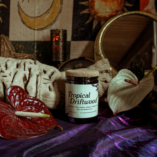Jar labeled 'Tropical Driftwood' on a mystical table with candles and decorative items.