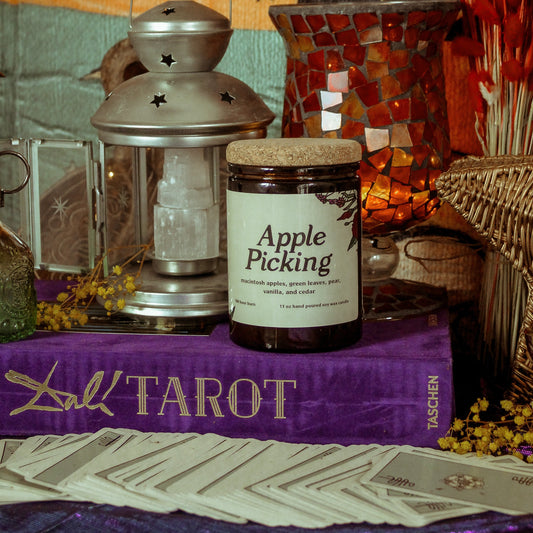 Jar labeled 'Apple Picking' on a tarot table with lantern and colorful backdrop